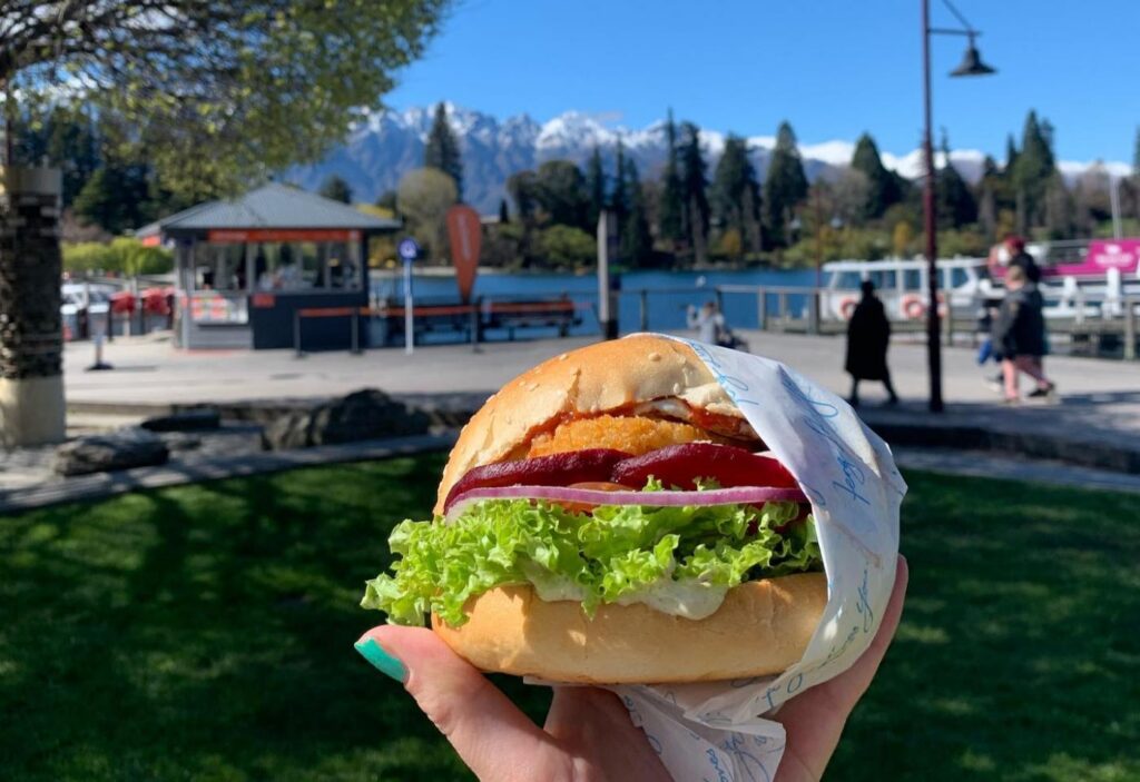 手持 Fergburger 汉堡，背景是湖泊与山脉